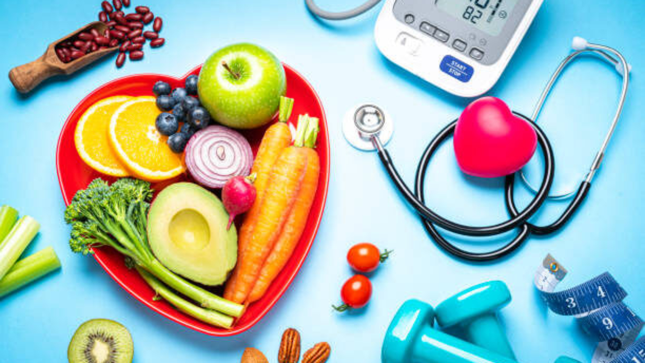 Healthy lifestyle concepts: red heart shape plate with fresh organic fruits and vegetables shot on blue background. A digital blood pressure monitor, doctor stethoscope, dumbbells and tape measure are beside the plate  This type of foods are rich in antioxidants and flavonoids that prevents heart diseases, lower cholesterol and help to keep a well balanced diet. High resolution 42Mp studio digital capture taken with SONY A7rII and Zeiss Batis 40mm F2.0 CF lens