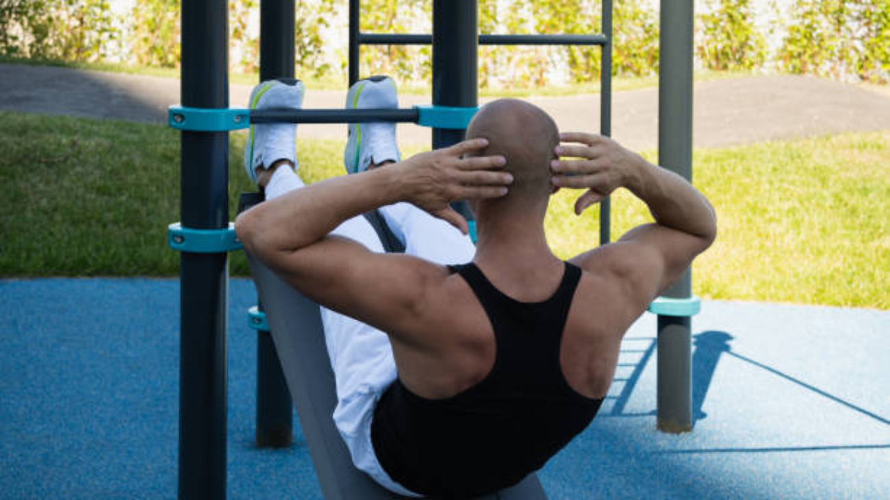 Athlete handsome male make fitness exercises and pumps up abs on street sports ground. Workouts and morning routines. Public sports field at modern city.
