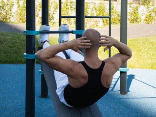 Athlete handsome male make fitness exercises and pumps up abs on street sports ground. Workouts and morning routines. Public sports field at modern city.