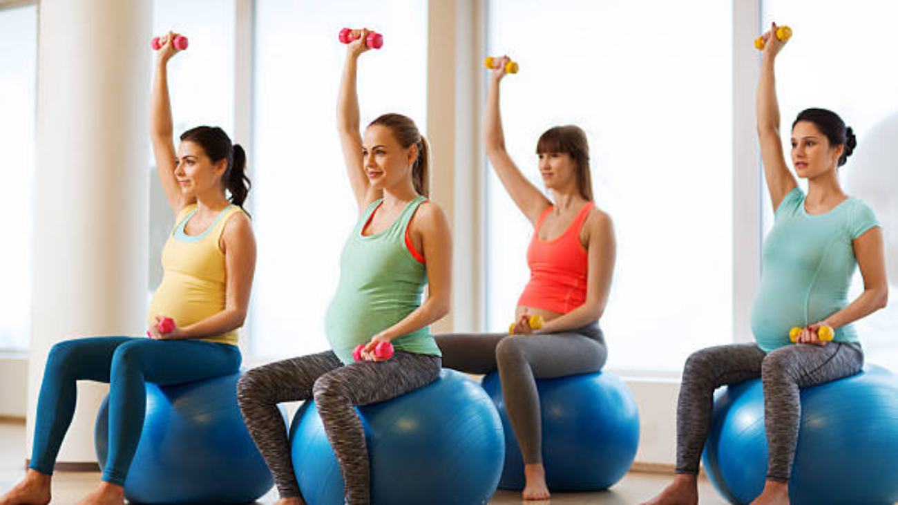 pregnancy, sport, fitness, people and healthy lifestyle concept - group of happy pregnant women with dumbbells exercising on ball in gym